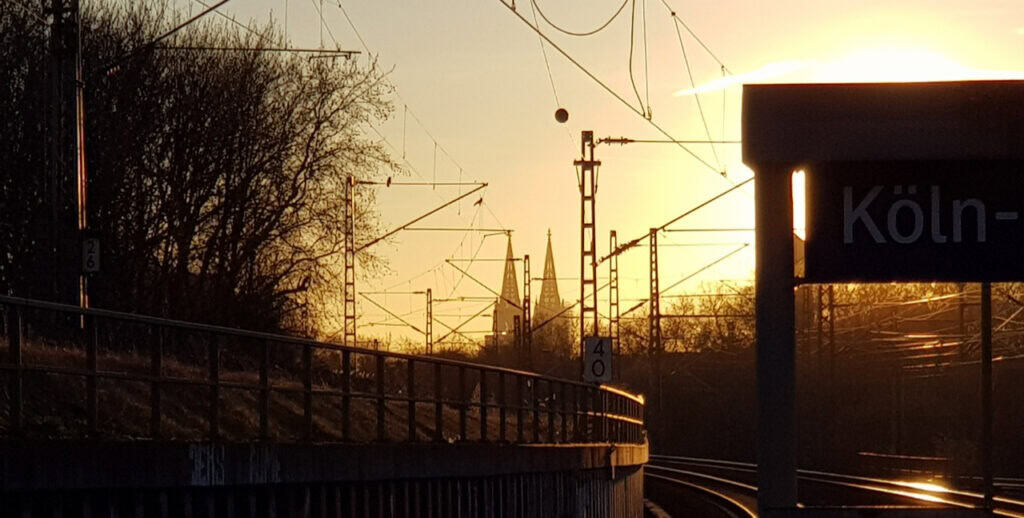 Bahnstrecke bei Sonnenuntergang mit sichtbarem Bahnhofsschild Köln.